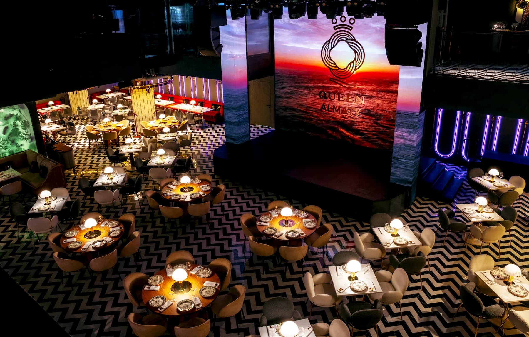 Queen event hall with formal table settings and a large digital stage