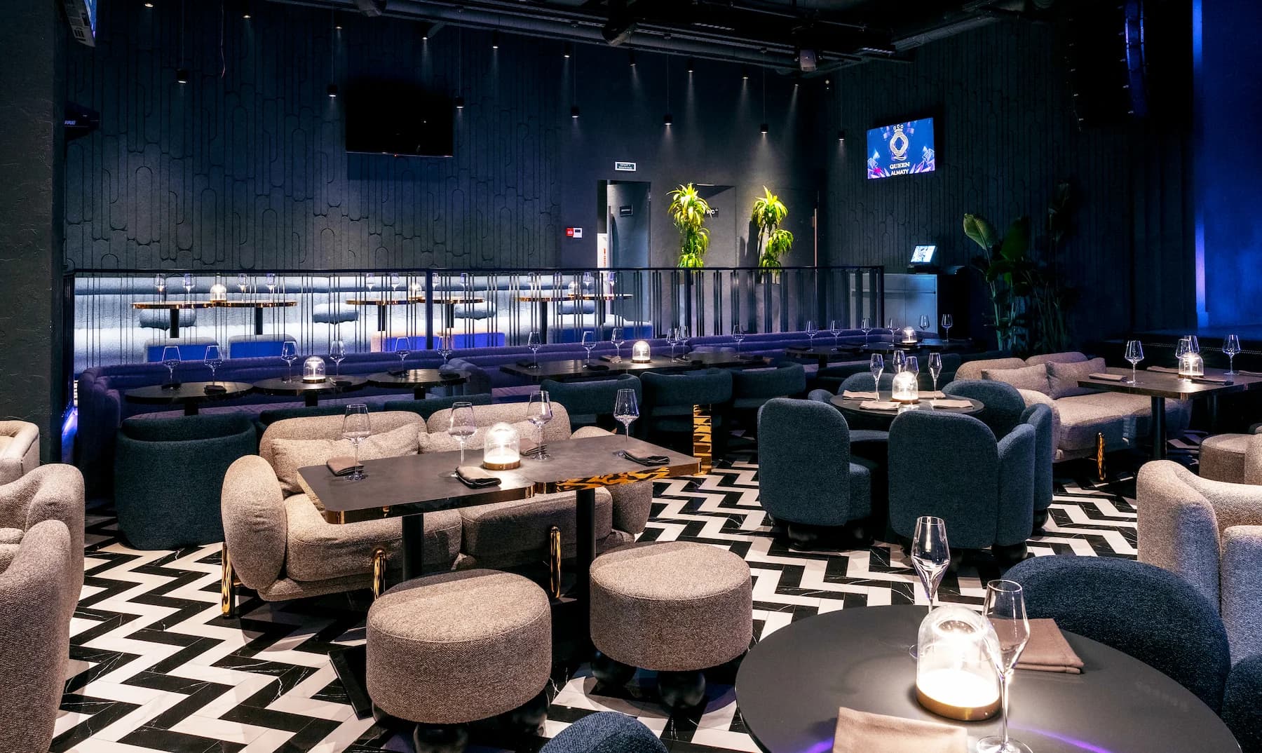 Dark karaoke lounge with upholstered seating, planted partitions and blue accent lighting