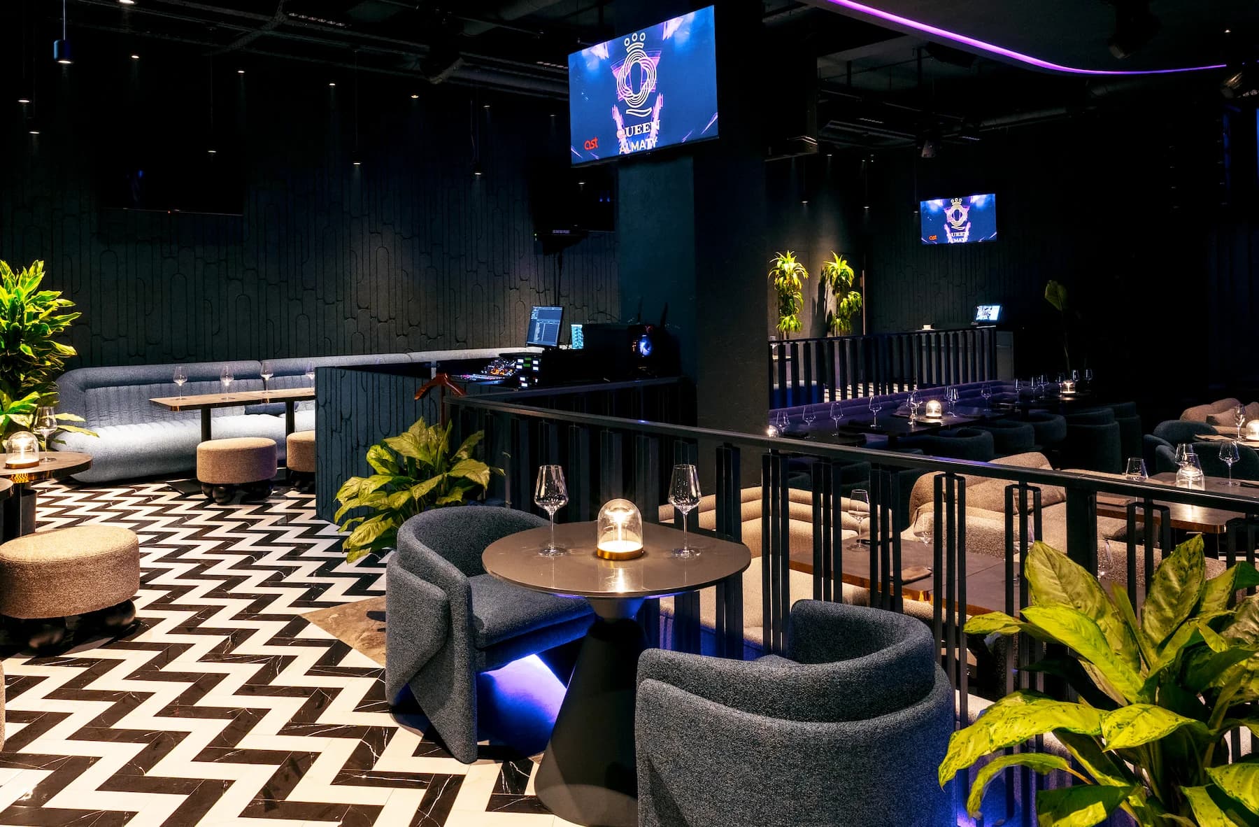 Dark social lounge with curved sofas, small tables and theatrical blue light