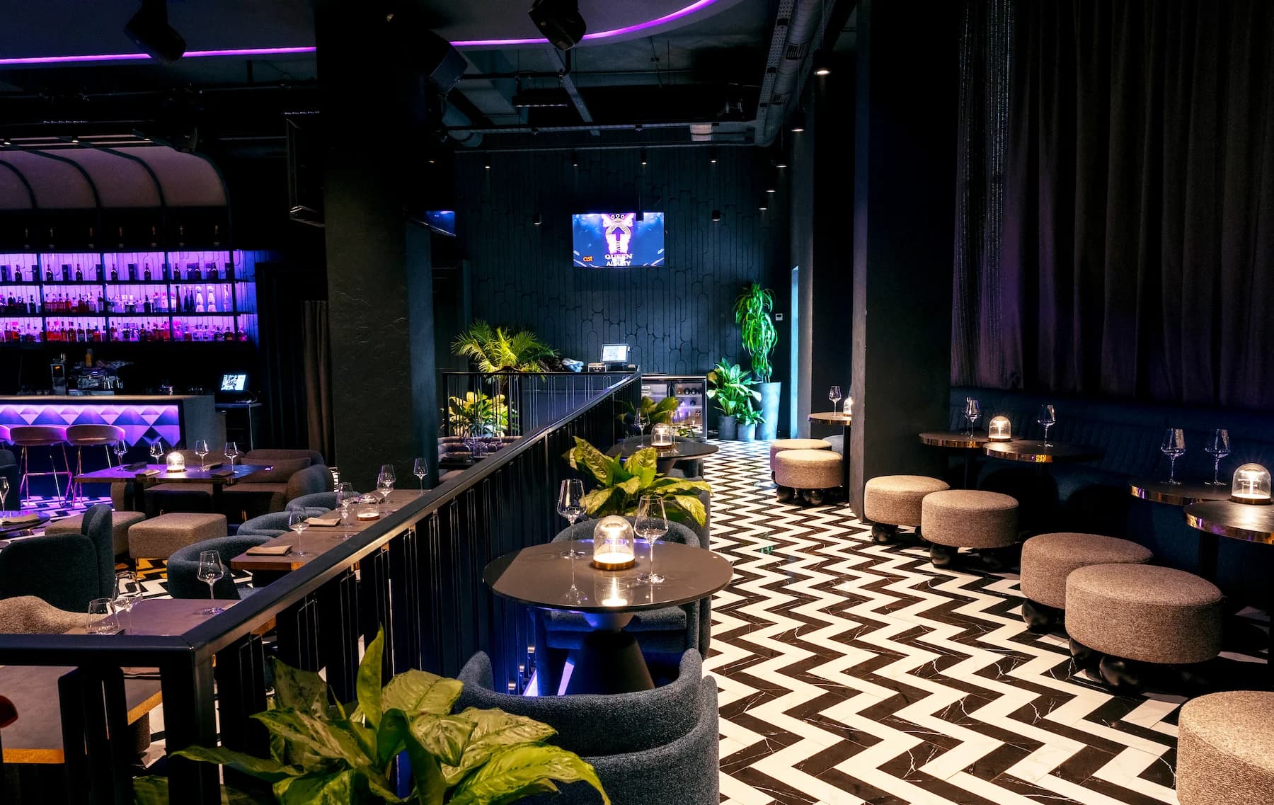 Queen karaoke interior with digital screens, planted railings and dark furniture