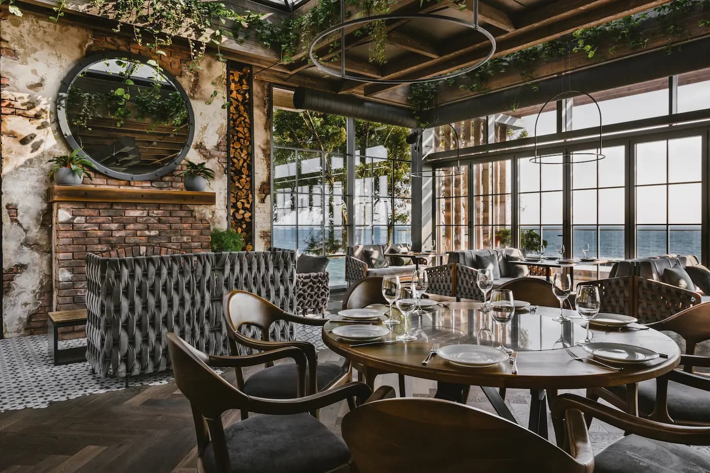 Sunlit restaurant lounge with upholstered seating, floor-to-ceiling windows and abundant suspended greenery.