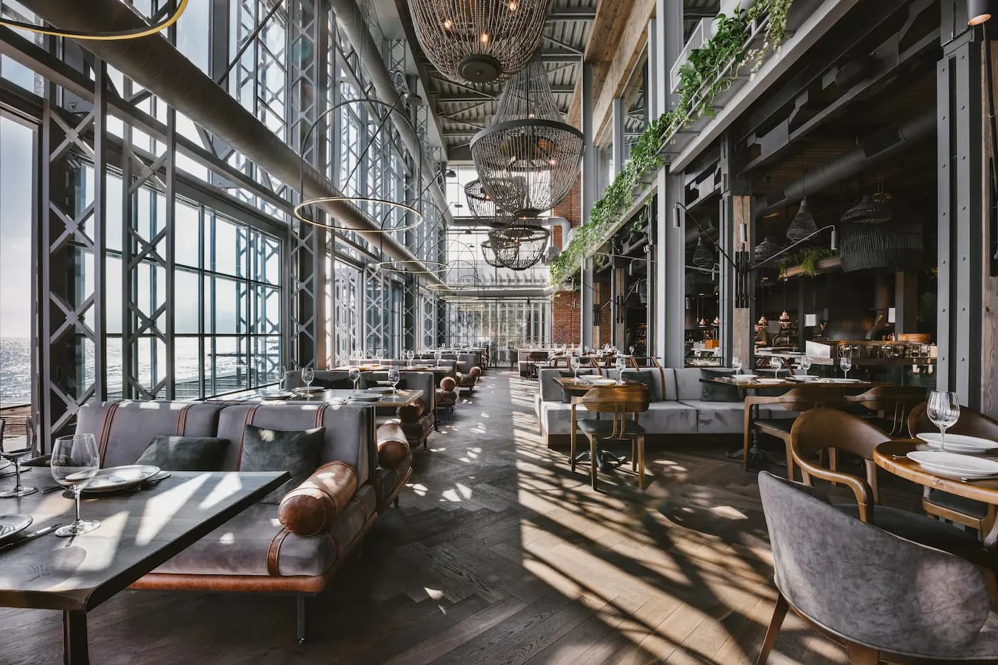 Central passage through the double-height dining hall with panoramic glazing, hanging plants and layered lighting.