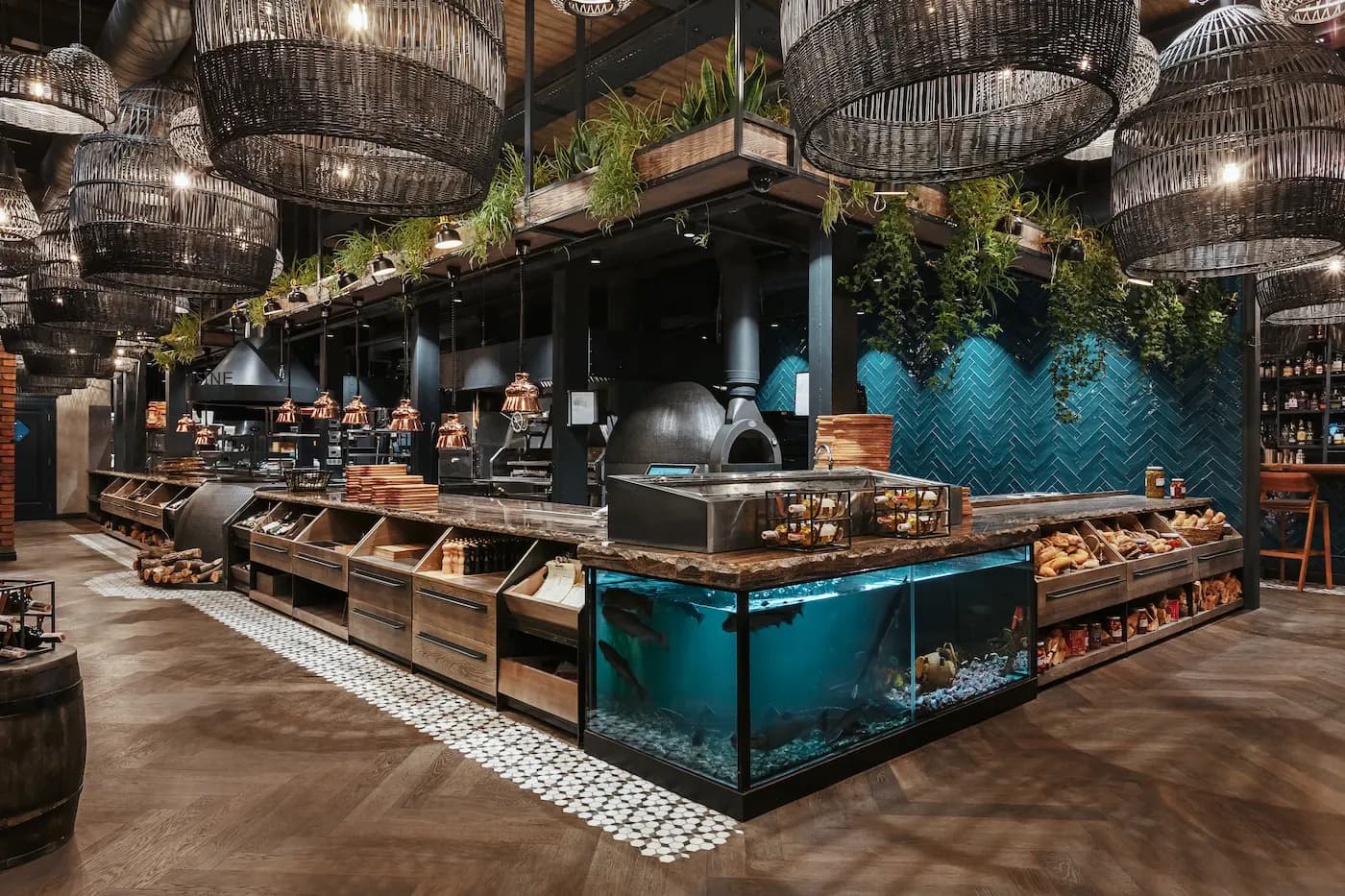Open kitchen and turquoise-tiled counter beneath a sculptural black canopy and cascading greenery.