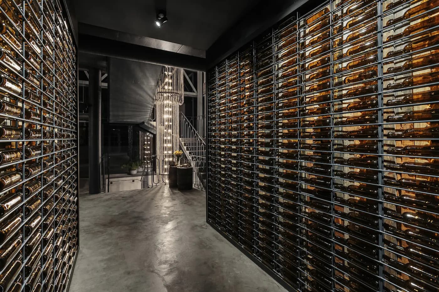 Wine corridor with floor-to-ceiling bottle racks, dark metal framing and a polished concrete floor.