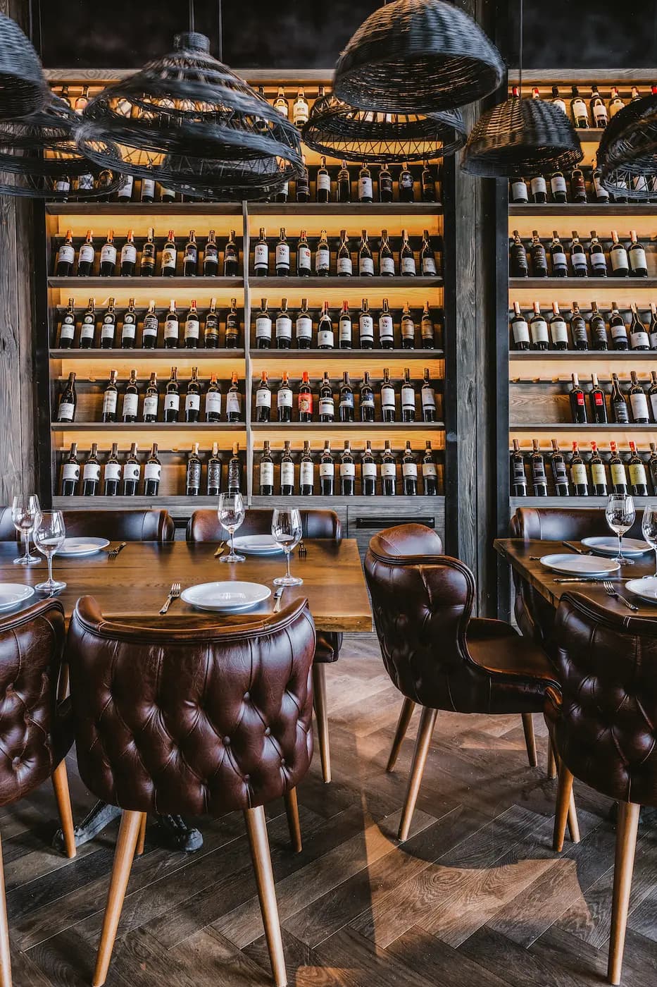 Leather dining area set against floor-to-ceiling illuminated wine shelves.