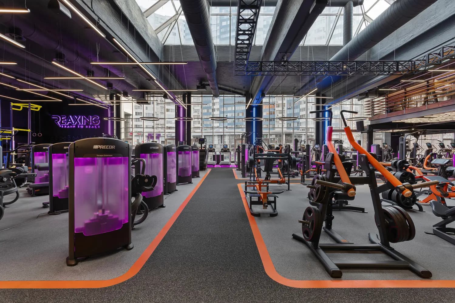 Daylit training floor with cardio machines, free weights and exposed industrial ceiling structures.