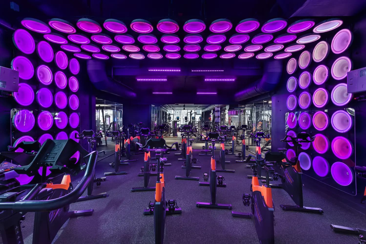 Group exercise studio illuminated by a grid of violet circular ceiling lights.