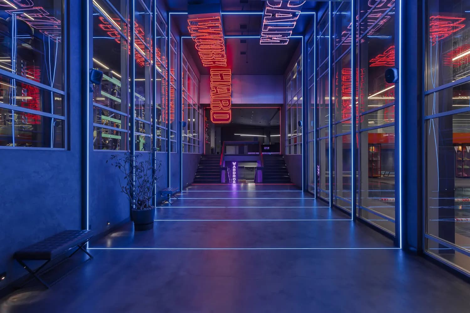 Glass-enclosed training studio with illuminated floor markers and red-blue neon reflections.
