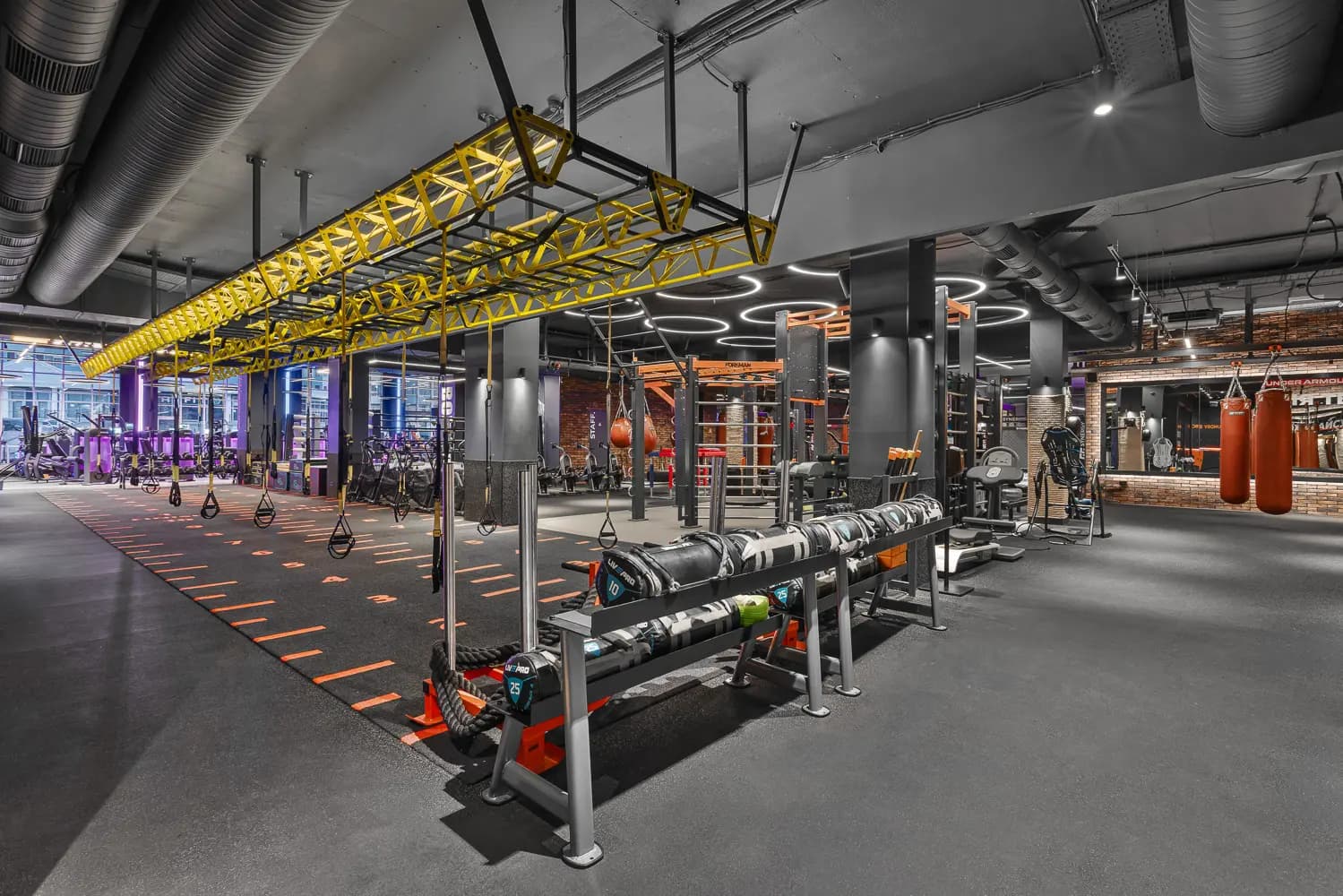 Strength-training station beneath a yellow overhead frame with dark equipment and orange graphics.