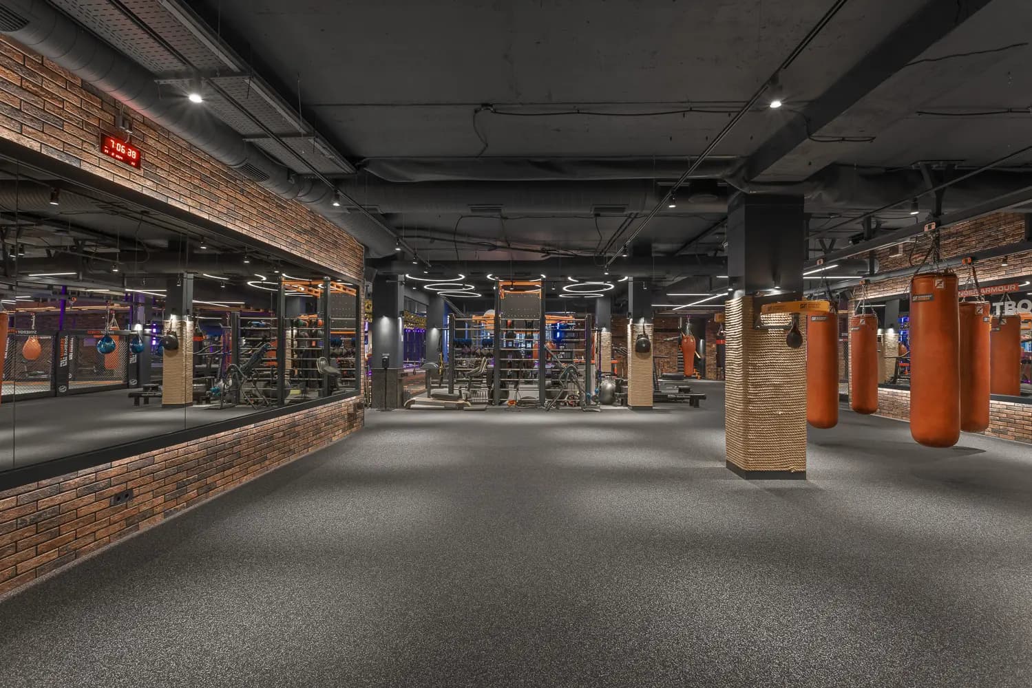 Wide view of the boxing area with heavy bags, training ring and industrial lighting.