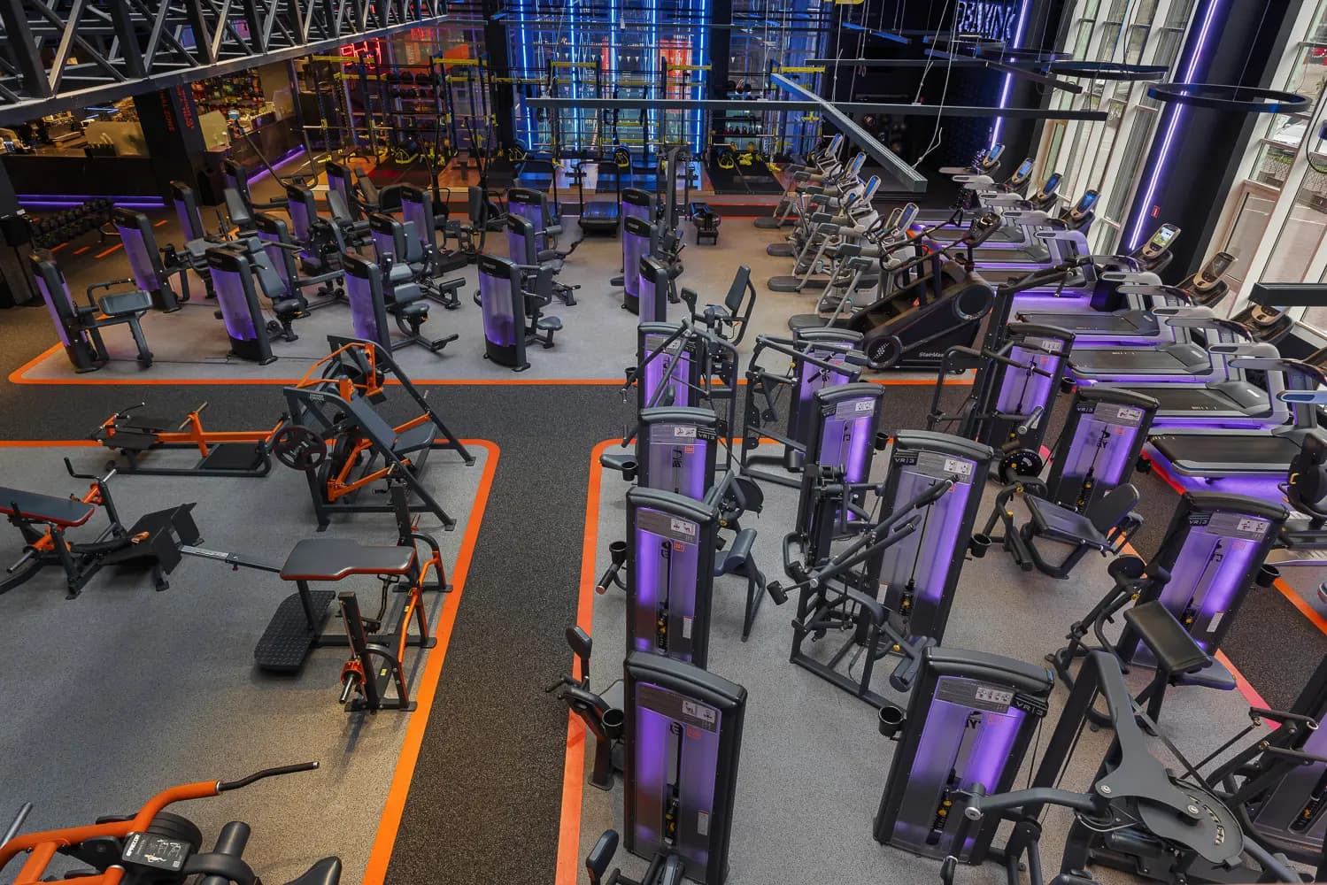 Elevated view across the open gym with densely arranged equipment and orange floor graphics.