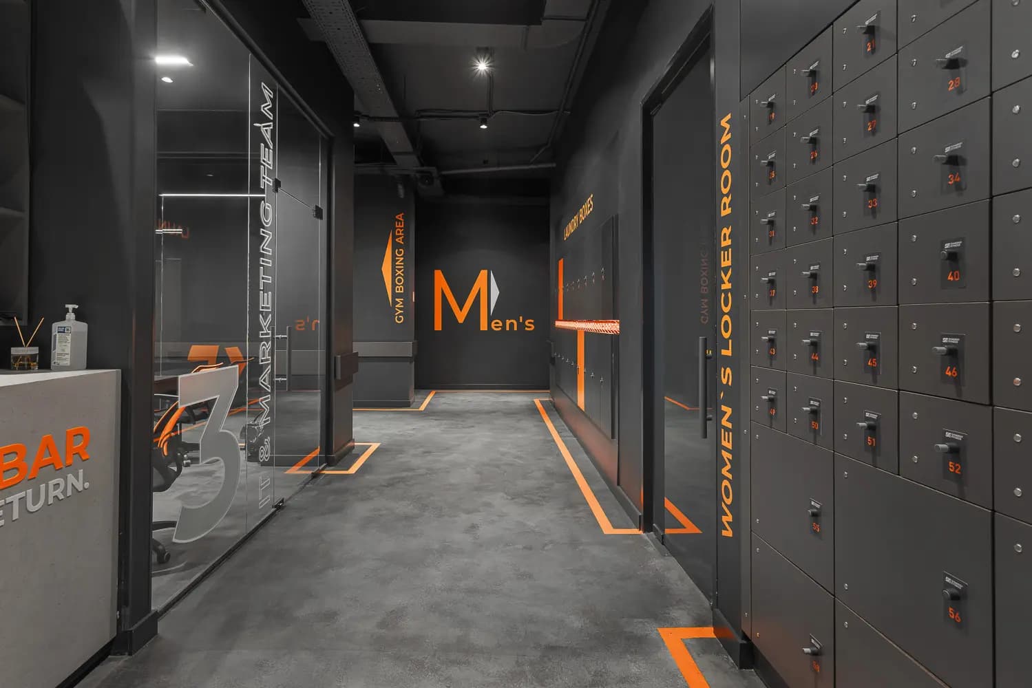 Locker-room corridor with dark storage units, orange edging and illuminated wayfinding.
