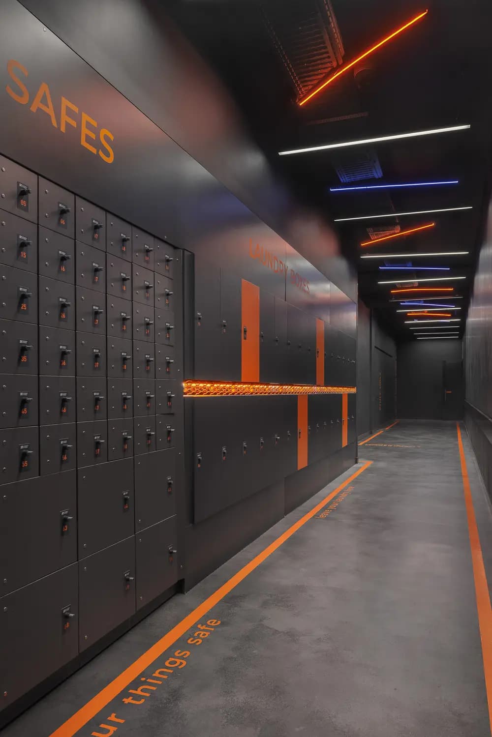 Changing-room passage with grey lockers, an orange bench and coloured ceiling lighting.