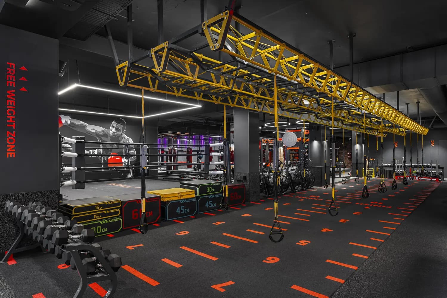 Functional training area with a suspended yellow rig and numbered orange floor markings.