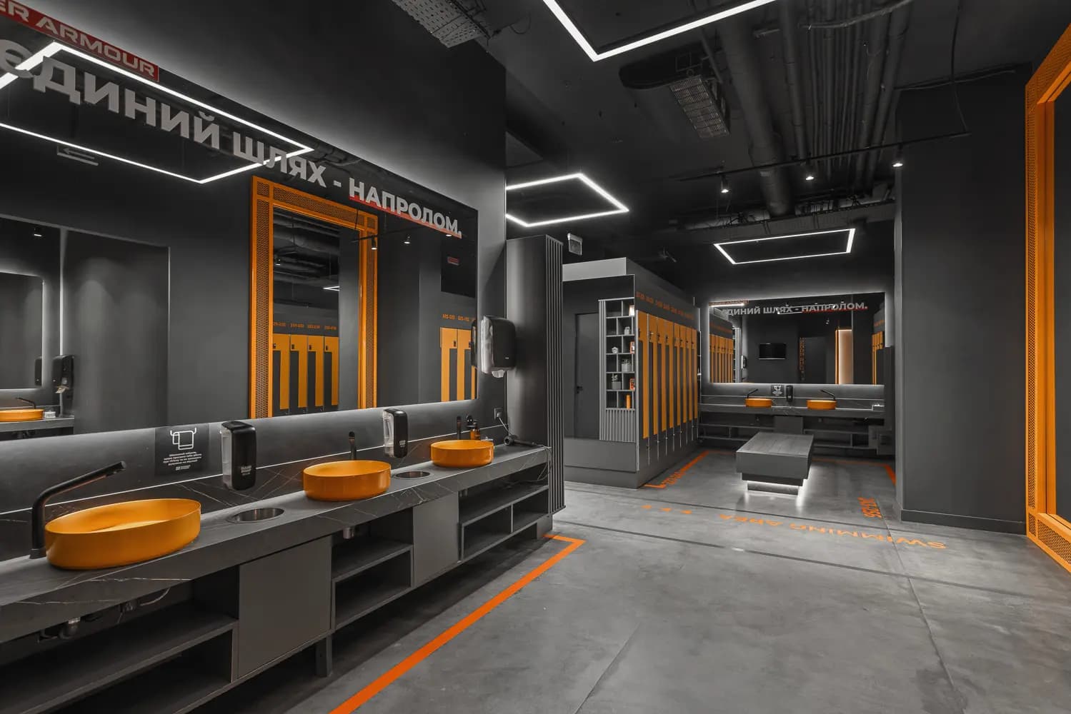 Locker room with black vanity counters, orange-framed mirrors and linear ceiling lights.