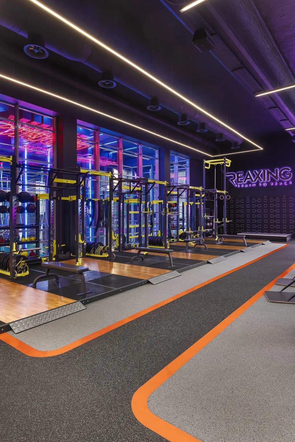 Glass-enclosed workout studio with neon lighting and orange perimeter markings.