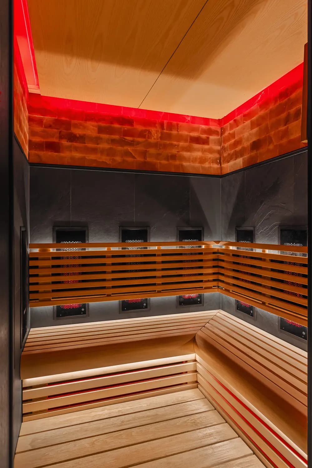 Timber sauna with stepped benches and red ambient ceiling lighting.