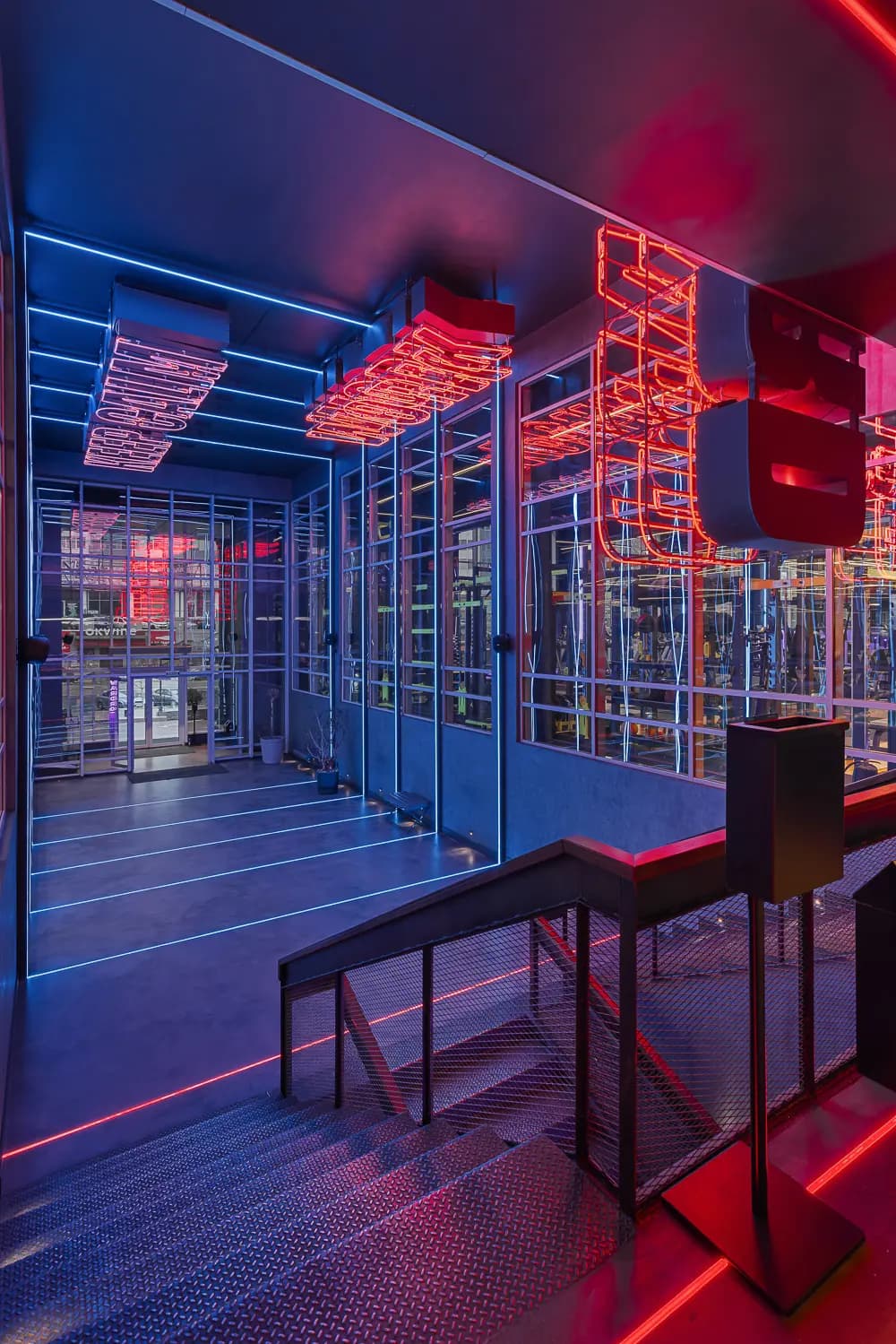 Neon-lit glass corridor viewed from the staircase landing.